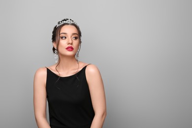 Beautiful young woman wearing luxurious tiara on light grey background, space for text