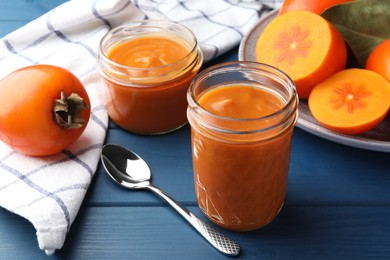 Photo of Delicious persimmon jam in glass jars served on blue wooden table, closeup