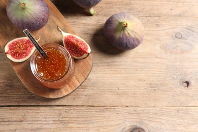 Glass jar with tasty sweet jam and fresh figs on wooden table, flat lay. Space for text