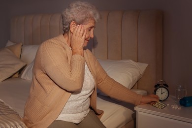 Photo of Elderly woman suffering from insomnia taking pills on bed at night