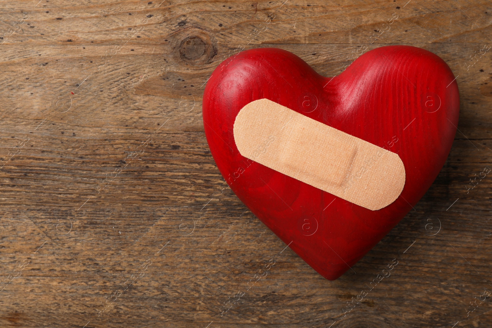 Photo of Top view of heart with medical patch on wooden background, space for text. Relationship problems concept