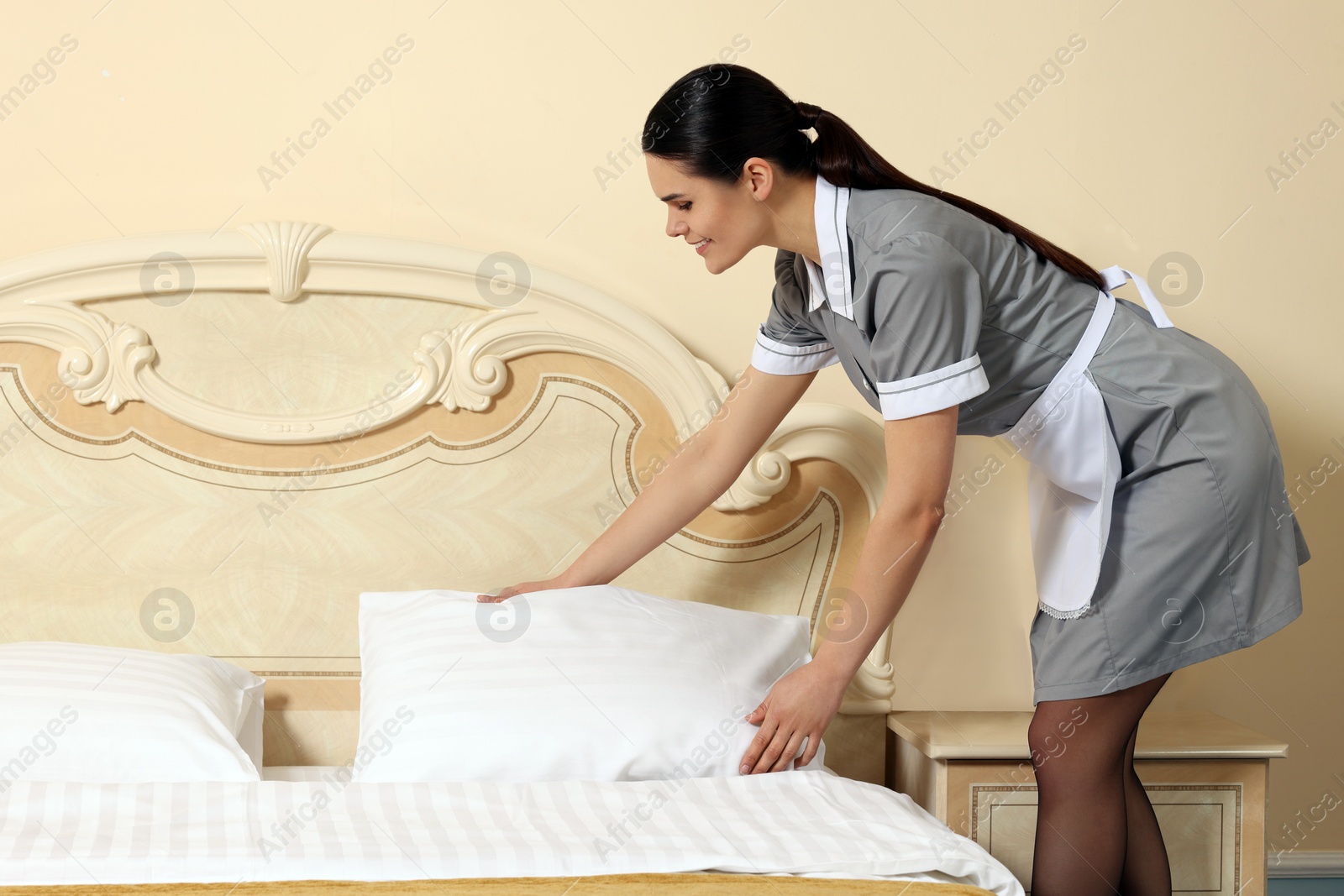 Photo of Young chambermaid making bed in hotel room. Space for text