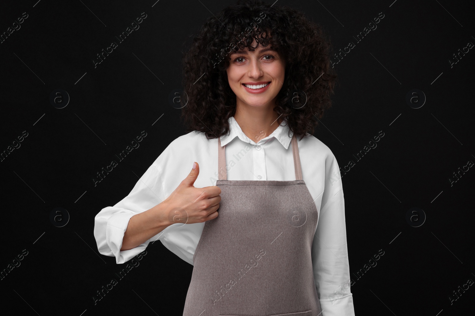 Photo of Happy woman wearing kitchen apron and showing thumbs up on black background. Mockup for design