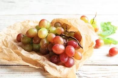 Photo of Fresh ripe juicy grapes and paper on wooden table