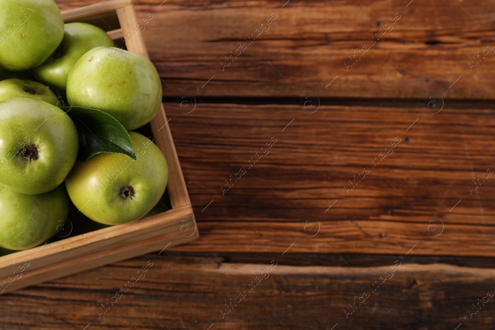 Photo of Fresh ripe green apples in crate on wooden table, above view. Space for text