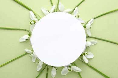 Frame of beautiful snowdrops around paper card on light background, flat lay. Space for text