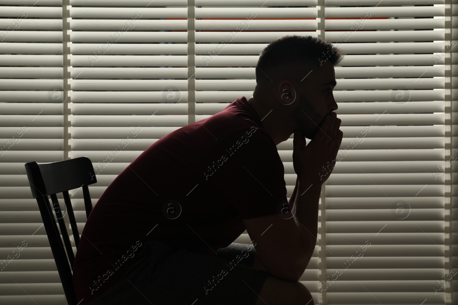 Photo of Sad man sitting near closed blinds indoors