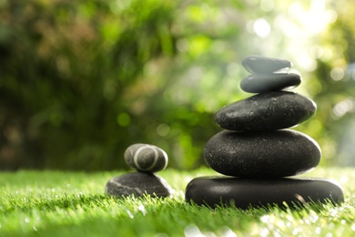 Photo of Stacks of stones on green grass against blurred background, space for text. Zen concept
