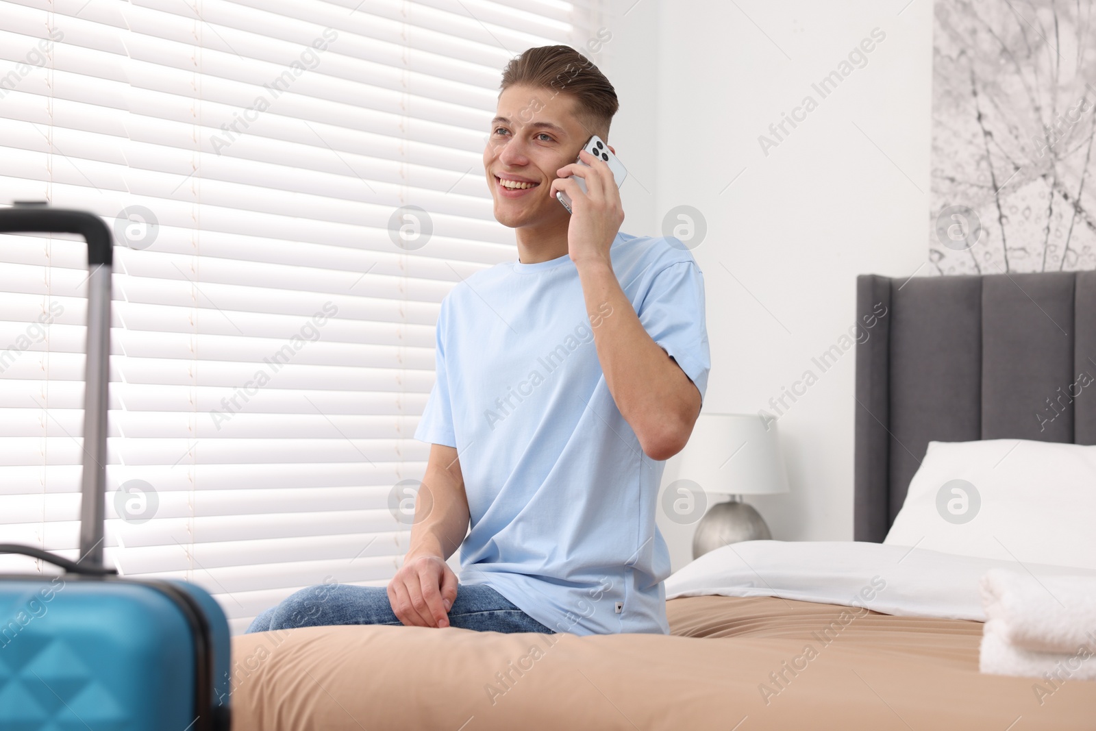 Photo of Smiling guest talking by smartphone on bed in stylish hotel room