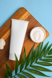 Photo of Different cosmetic products, palm leaf and shell on light blue background, flat lay