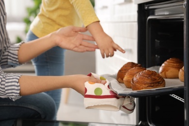 Photo of Mother and daughter taking out buns from oven in kitchen