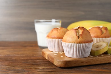 Tasty muffins served with banana on wooden table. Space for text