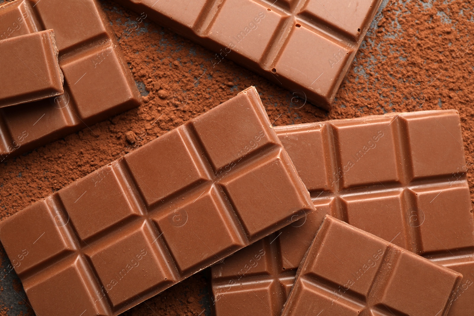 Photo of Delicious milk chocolate and cocoa powder on grey table, flat lay