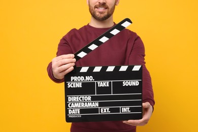 Photo of Smiling actor holding clapperboard on orange background, closeup