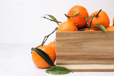 Wooden crate with fresh ripe tangerines and leaves on white table, closeup. Space for text