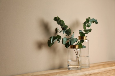 Beautiful eucalyptus branches in glass vases on wooden table against beige background. Space for text