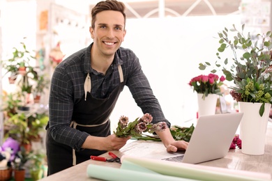 Photo of Young florist working with laptop in flower shop