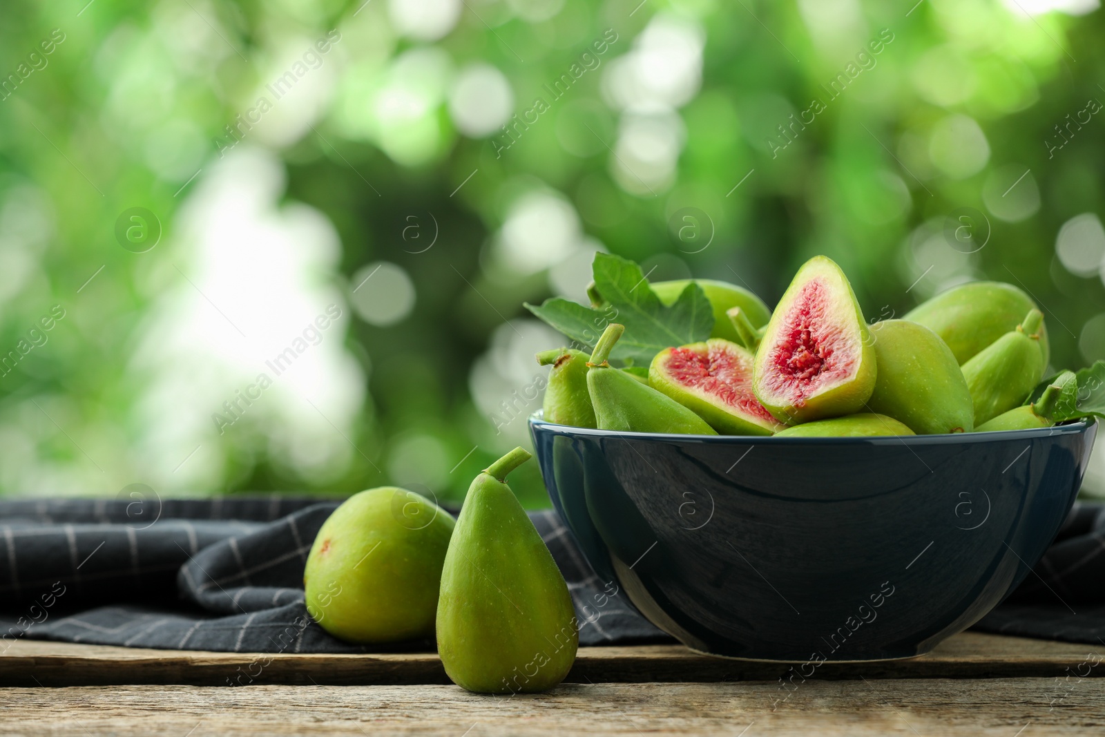 Photo of Cut and whole green figs on wooden table against blurred background, space for text