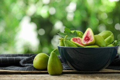 Photo of Cut and whole green figs on wooden table against blurred background, space for text