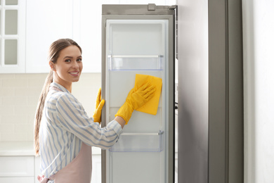 Photo of Woman in rubber gloves cleaning refrigerator at home