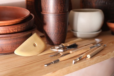 Photo of Set of different crafting tools and clay dishes on wooden table in workshop, closeup