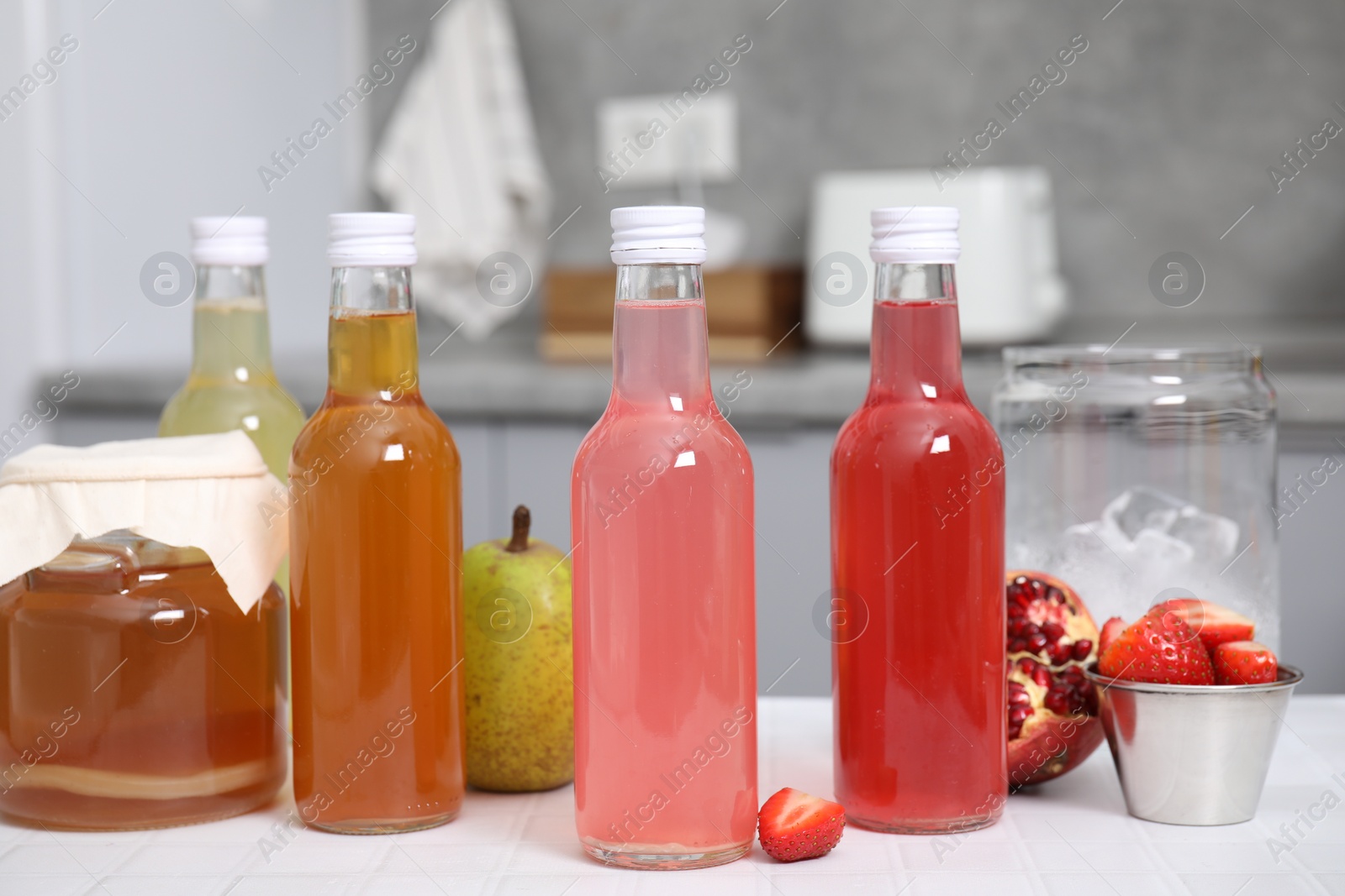 Photo of Tasty kombucha in glass bottles, jar and fresh fruits on white tiled table