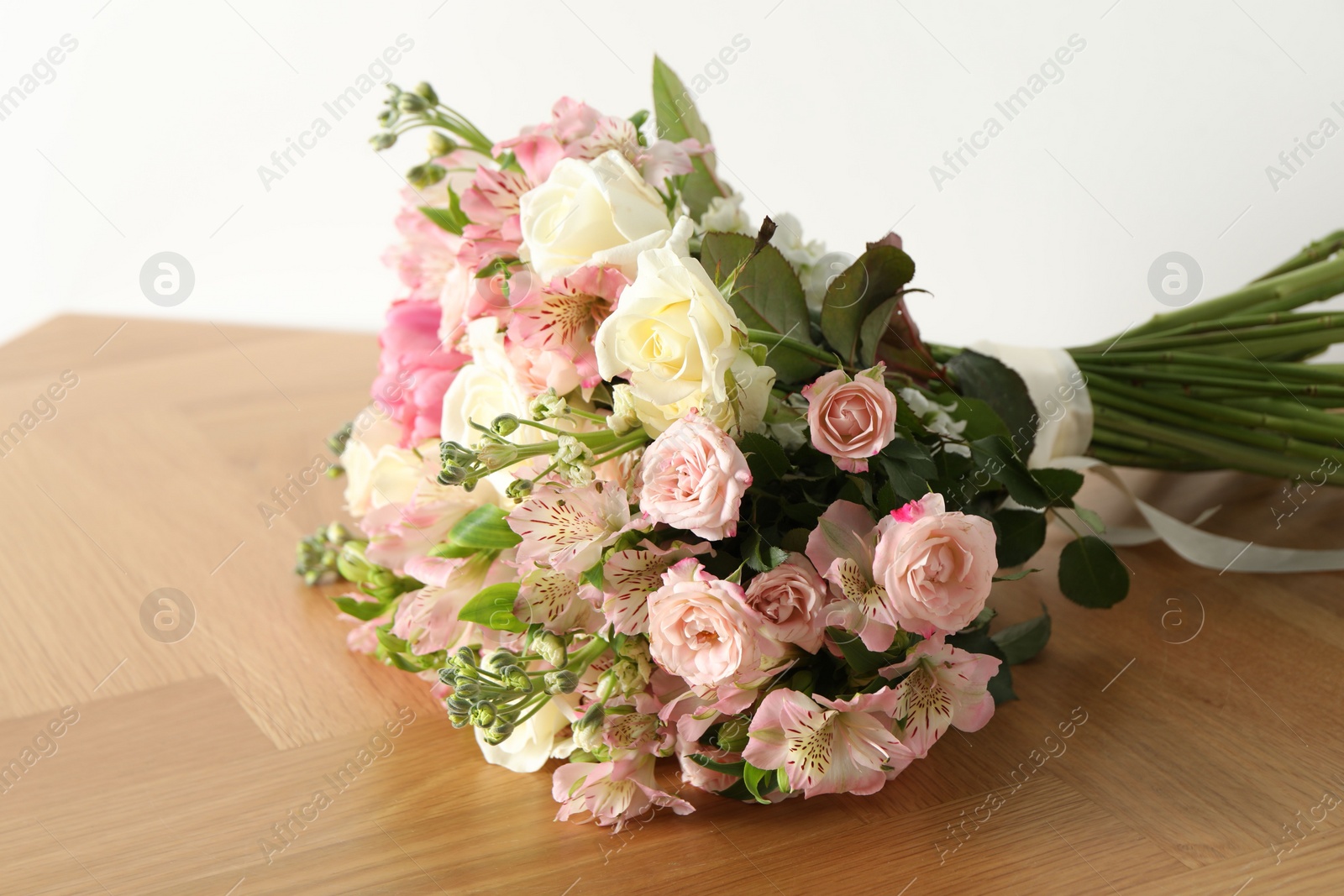 Photo of Beautiful bouquet of fresh flowers on wooden table near white wall