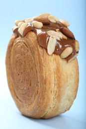 Photo of One supreme croissant with chocolate paste and nuts on light blue background, closeup. Tasty puff pastry