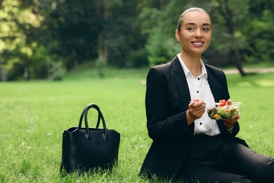 Photo of Lunch time. Happy businesswoman with container of salad on green grass in park