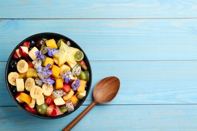 Photo of Delicious exotic fruit salad and spoon on light blue wooden table, flat lay. Space for text