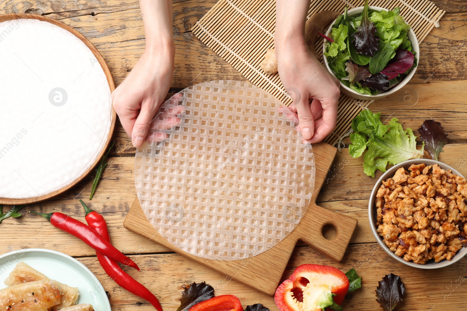 Photo of Woman making tasty spring roll at wooden table, top view