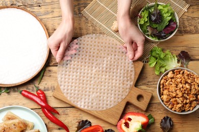 Woman making tasty spring roll at wooden table, top view