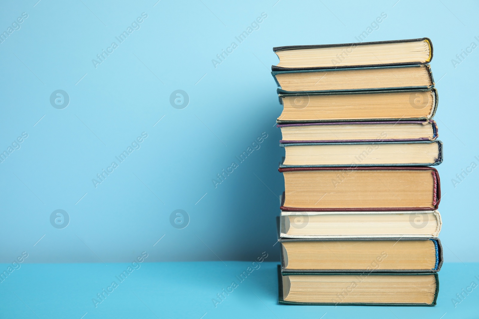 Photo of Stack of hardcover books on light blue background, space for text