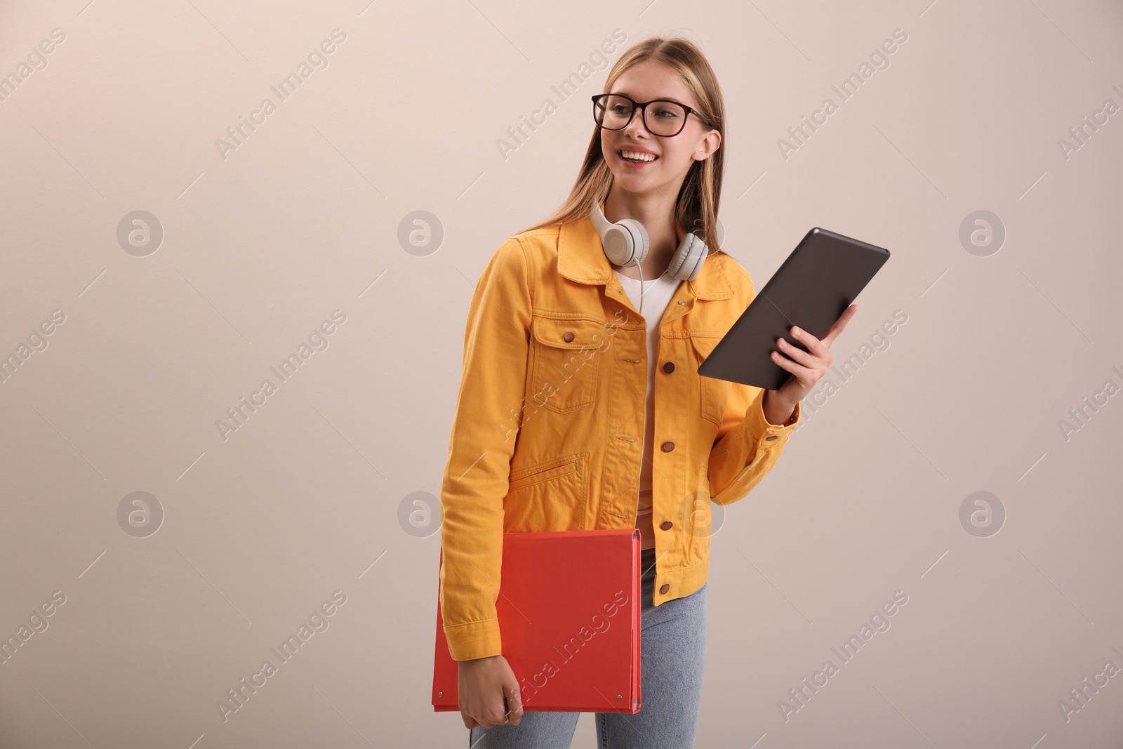 Photo of Teenage student with tablet, folder and headphones on beige background