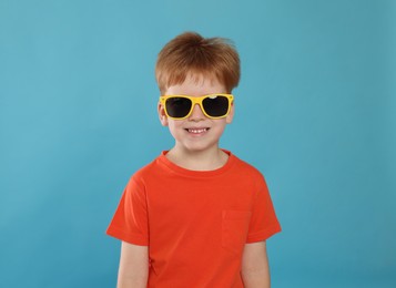 Photo of Cute little boy with sunglasses on light blue background