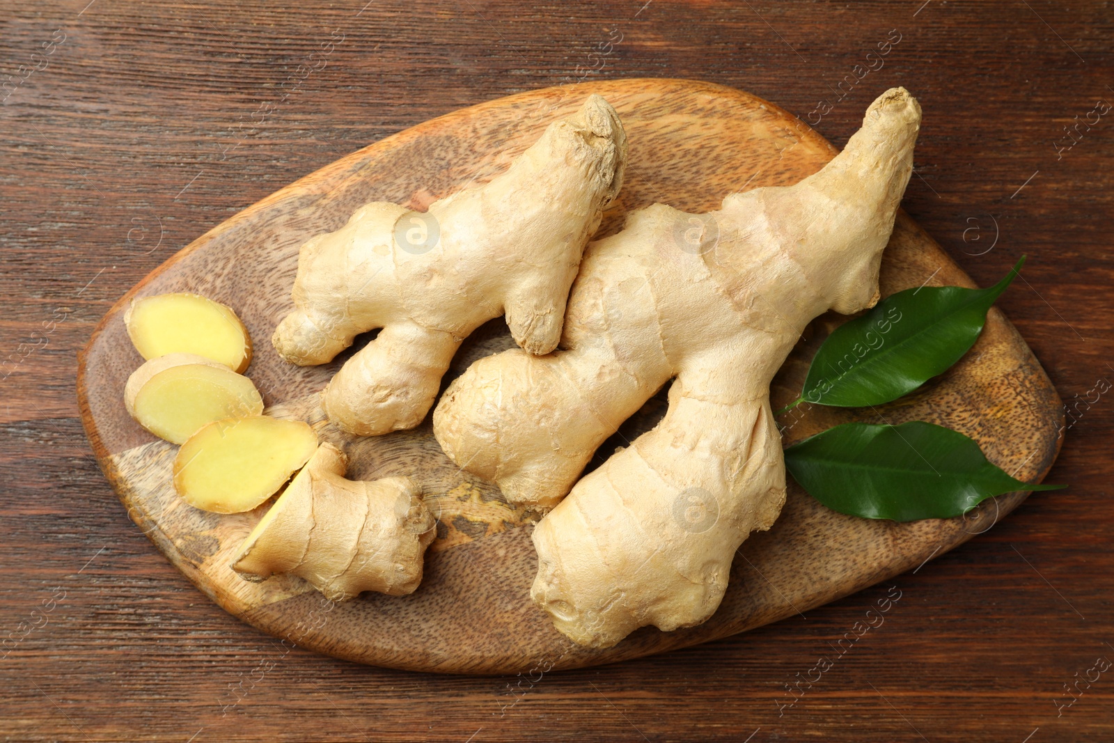 Photo of Cut and whole fresh ginger with leaves on wooden table, top view