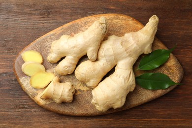 Photo of Cut and whole fresh ginger with leaves on wooden table, top view