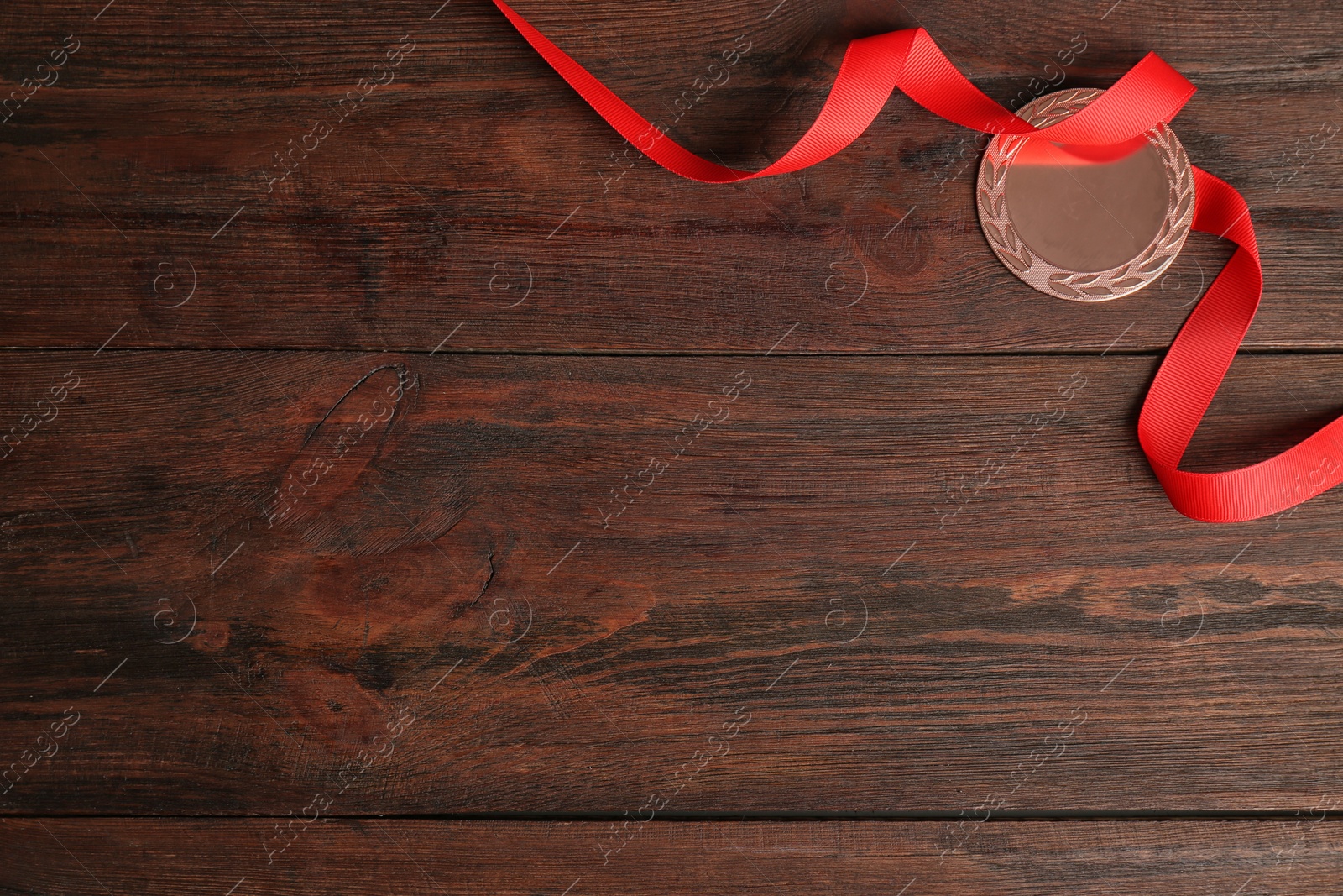 Photo of Bronze medal with red ribbon on wooden background, flat lay. Space for design