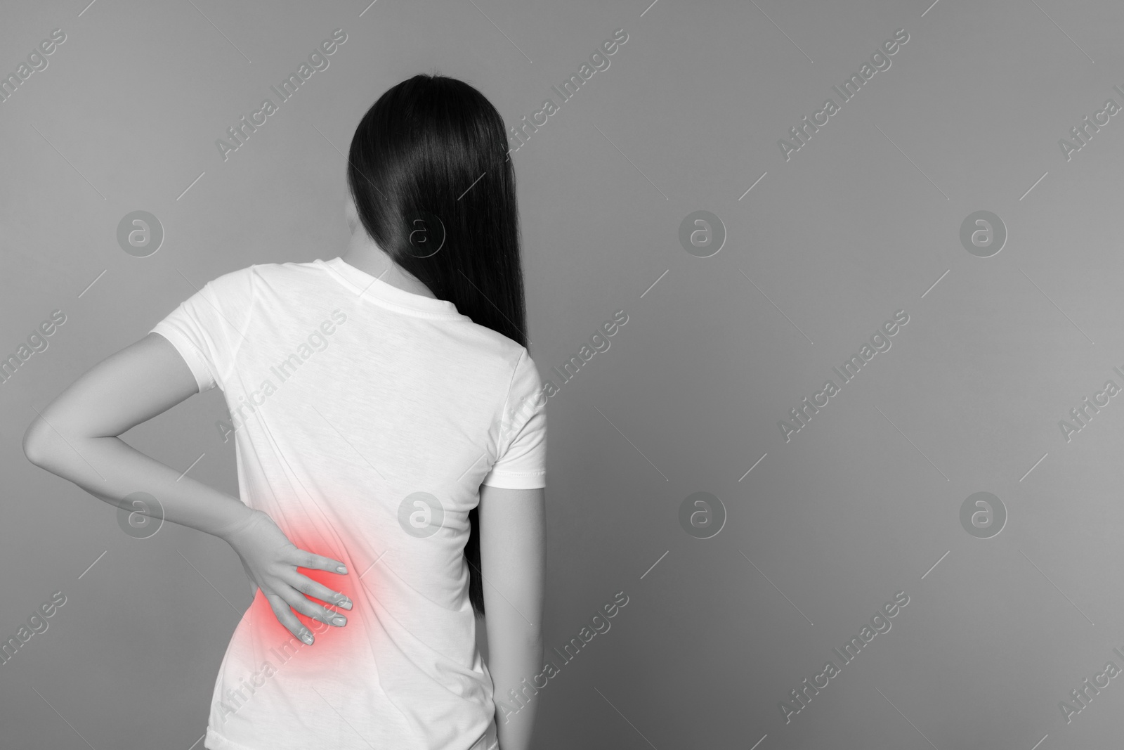 Image of Woman suffering from back pain on grey background. Black and white effect with red accent