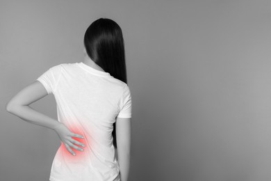 Woman suffering from back pain on grey background. Black and white effect with red accent