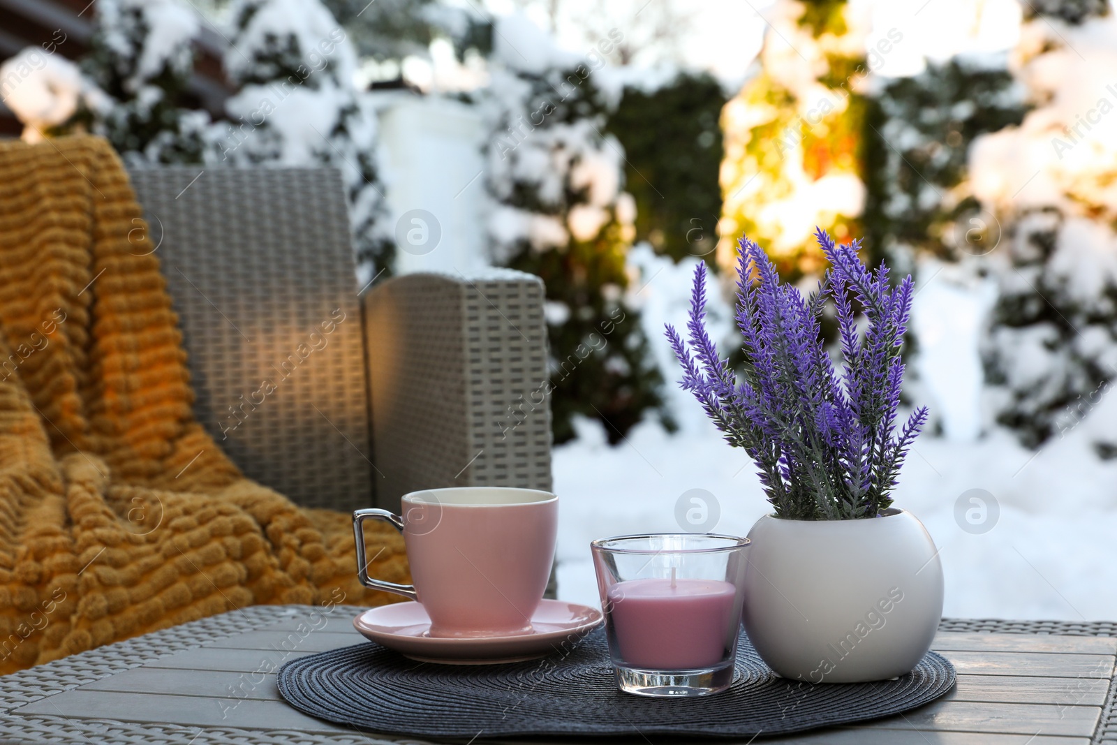 Photo of Candle, potted flowers and cup of hot drink on coffee table outdoors. Cosy winter