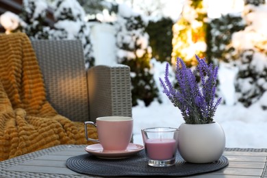 Photo of Candle, potted flowers and cup of hot drink on coffee table outdoors. Cosy winter