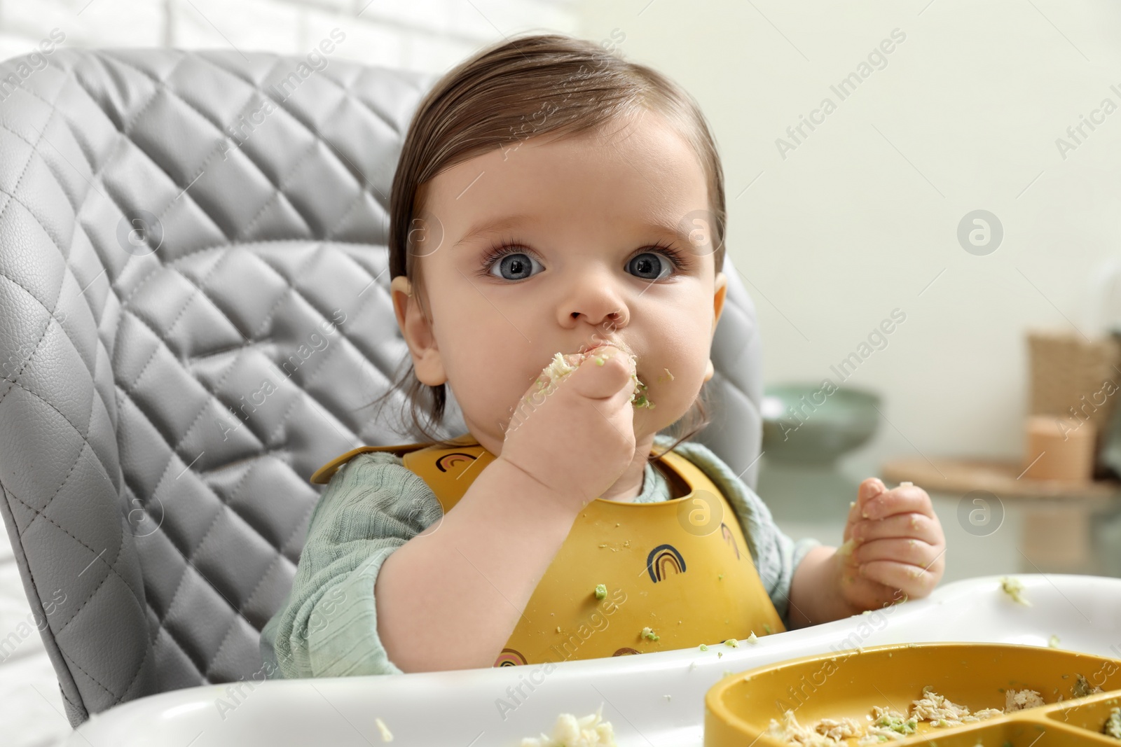 Photo of Cute little baby eating healthy food in high chair indoors