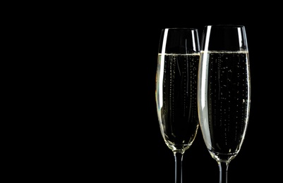 Photo of Glasses of champagne on black background, space for text