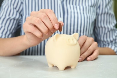 Photo of Woman putting coin into piggy bank at light table, closeup