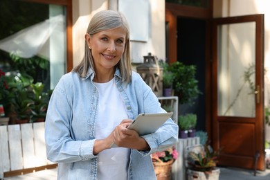 Photo of Happy business owner using tablet near her flower shop outdoors, space for text