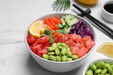 Photo of Poke bowl with salmon, edamame beans and vegetables on white marble table