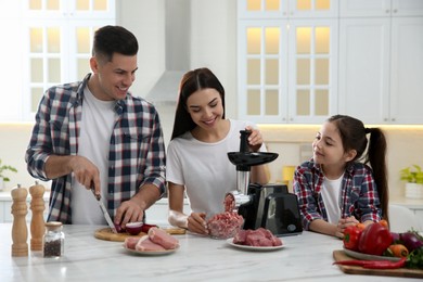 Photo of Happy family making dinner together in kitchen, woman using modern meat grinder while man cutting onion