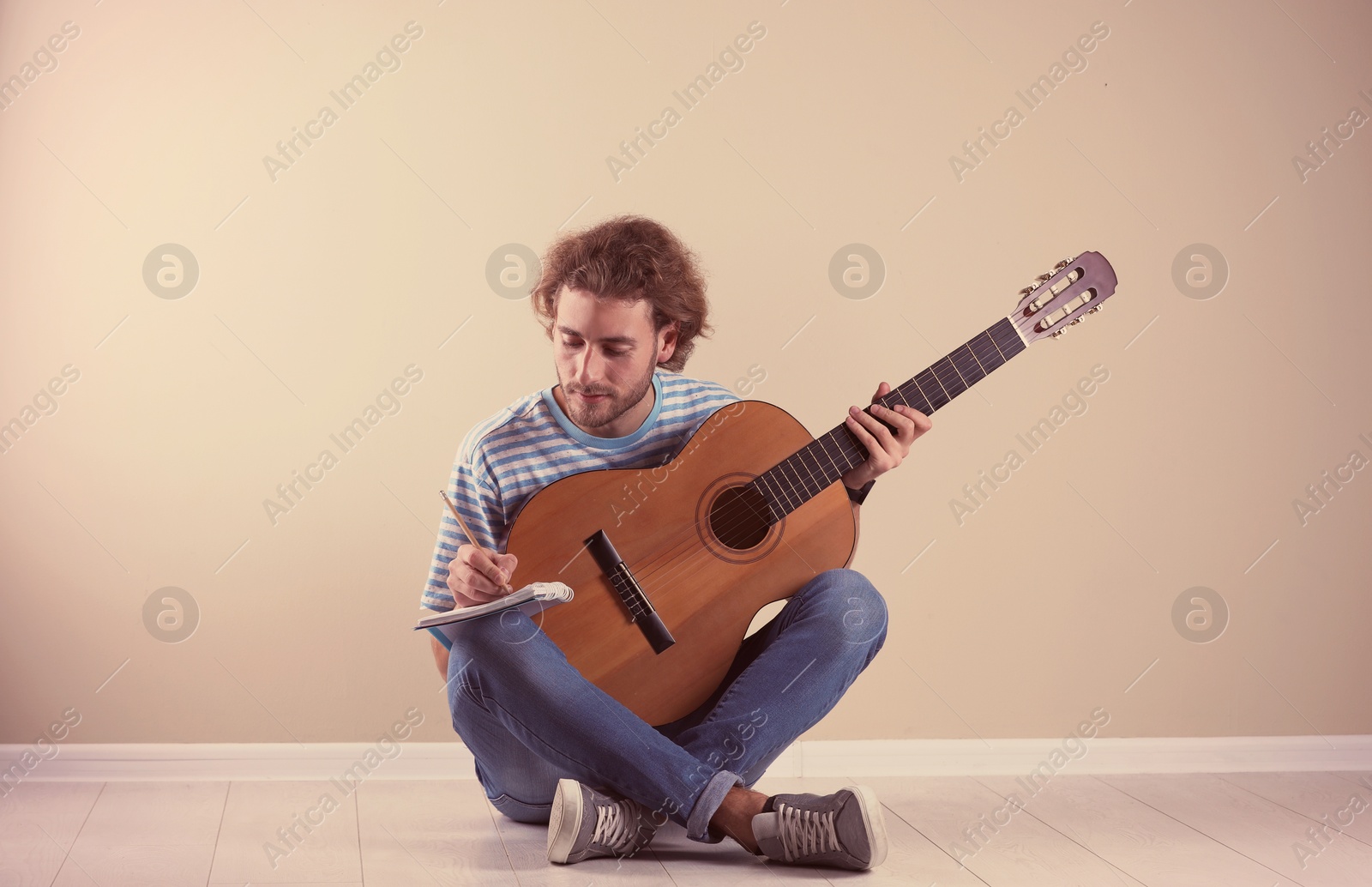 Photo of Young man with acoustic guitar composing song near grey wall