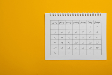 Photo of Paper calendar on yellow background, top view. Space for text
